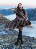 Model spinning in raccoon fur coat on mountain cliff, showcasing coat's volume and luxurious texture in winter fashion setting.