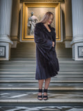 Woman in a black fur coat standing in an elegant interior setting with classical architecture.