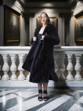 Woman in a dark coat standing in an elegant interior setting with classical architecture.
