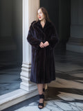 Woman wearing a dark fur coat standing in an elegant interior setting.