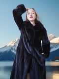 Woman in a fur coat standing in front of mountains and water