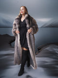 Woman wearing a long fur coat standing against a reflective surface.
