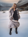 Woman in a fur coat standing in a snowy landscape with mountains in the background