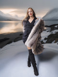 Woman in a dark dress and fur coat standing in a snowy landscape with mountains.