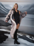 Woman wearing a long fur coat with a black dress and boots on a neutral background