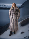 Person wearing a fur coat standing on a snowy landscape with mountains in the background