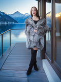Woman in a fur coat standing on a dock with mountains and water in the background