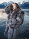 Woman in a fur coat standing by a lake with mountains in the background