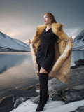 Woman in a fur coat standing in a snowy landscape with mountains and water.