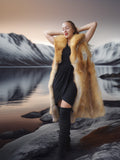 Woman in a fur vest standing in front of a mountainous landscape with a lake.