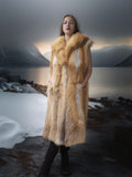 Person wearing a fur coat standing in a snowy landscape with mountains in the background