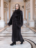 Model walks confidently in full-length black mink coat, styled for upscale winter fashion in a neoclassical setting.