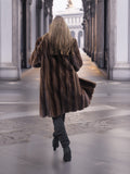 Back view of woman walking in dark mahogany mink fur coat, emphasizing the coat's full length and premium fur quality.