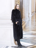 Model leaning against column in black mink fur coat with hands in pockets. Regal and warm outerwear for winter, size M.
