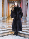 Model in black mink fur coat with hands in pockets, standing in ornate hall. Regal full-length fur outerwear for winter, size M.