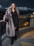 Woman in a fur coat standing on a balcony with mountain and cityscape background