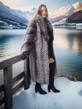 Woman in a fur coat standing by a snowy lake with mountains in the background
