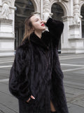 Elegant black mink fur coat with soft texture and wide collar, styled for upscale outerwear fashion in a classic architectural setting.