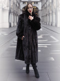 Model poses in a black mink fur coat with hands in pockets, showcasing the coat's rich texture and timeless elegance.