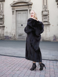 Elegant black mink fur coat with flared silhouette, worn by a stylish woman in front of a historic building.
