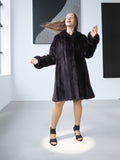 Woman wearing a black fur coat in a minimalistic room.