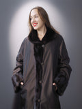 Woman wearing a long dark coat with fur trim against a gray background