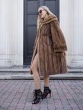 Elegant pastel brown mink fur coat with hooded design, worn by stylish woman against architectural building backdrop.