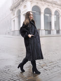 Model in black mink fur coat walking on cobblestone street, showcasing timeless elegance in luxury outerwear.