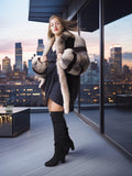 Woman in a fur coat and black dress standing on a balcony with city skyline view