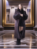 Woman in a long dark coat standing in a grand hall with marble floor and columns.