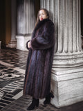 Woman in a long fur coat standing against classical architecture.