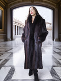 Woman wearing a long dark fur coat in an elegant interior setting with marble floors and classical architecture.