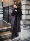 Woman in a fur coat standing on steps with a decorative metal railing in the background