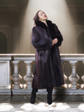 Woman wearing a fur coat standing in a grand hall with a spotlight on her.