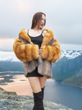 The Wild Muse red gray fox fur coat, styled with a black dress in a snowy fjord setting, showcasing its plush texture and elegance.