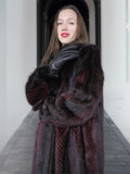 Model poses with gloved hand in red and black mink fur coat, emphasizing plush texture and luxury craftsmanship.