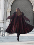 Back view of flowing two tone mink fur coat in red and black, showcasing full-length design and dramatic movement.