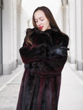 Model hugs herself in red and black mink fur coat, highlighting warmth and comfort of luxury winter outerwear.