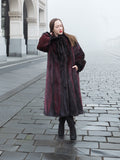 Model poses in red and black mink fur coat on cobblestone street, showcasing luxurious and warm full-length outerwear.