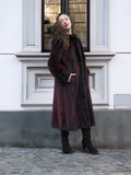 Model leans against building in red and black mink fur coat, showcasing elegant cold-weather fashion for women.