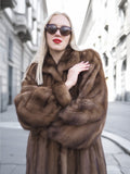 Elegant woman in pastel brown Canadian mink fur coat, sunglasses, red lipstick, and blonde hair strolling down the street.