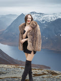 Model smiling in Raccoon Glamour Jacket - Mountain Mirage S/M with scenic fjord view, showcasing luxury fur outerwear in nature.