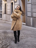 Golden Reverie M - Cozy blond mink coat with high collar, styled for winter elegance on a cobblestone street.