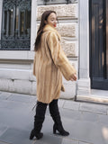 Golden Reverie M - Rear view of flowing mink coat in beige tones, styled with black boots for a chic urban look.