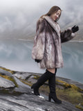 Soft and fluffy blue fox fur coat with oversized collar, worn while walking on rocky terrain. Real fur jacket for elegant winter fashion.
