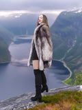 Plush soft blue fox coat with luxurious shawl collar, modeled above a scenic fjord. Real fur outerwear for stylish winter fashion.
