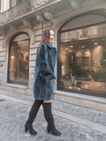 Side view of The Still Hour sheared muskrat fur coat in deep teal, worn with knee-high boots for a chic winter look.
