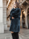 Side profile of The Still Hour sheared muskrat fur coat in deep teal, styled with black boots for a refined cold-weather look.