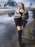 Woman in a fur coat standing on a reflective water surface with mountains in the background