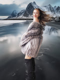 Woman in a fur coat standing on a reflective beach with mountains in the background